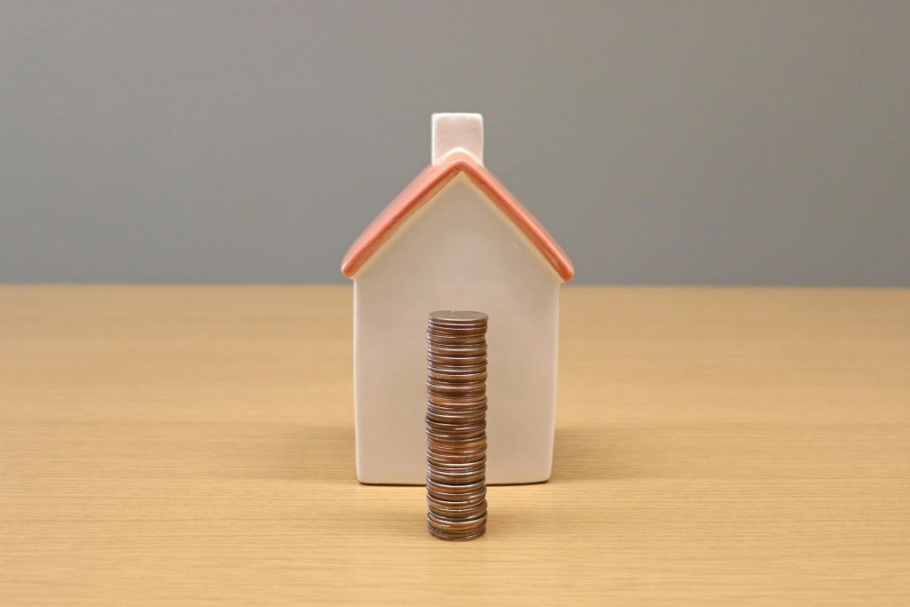 stacked coins in front of a miniature house
